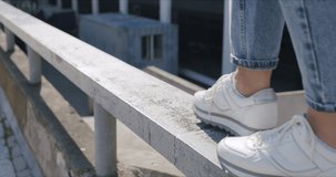 City urban lifestyle. Woman wearing in white sneakers and blue jeans goes on metallic railing.Girl walking and having fun on sunny day. 4K video slow motion 50 fps
