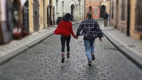 Sweet couple have romantic time while honeymoon trip in old european town. Young lovers holding hands running on street and kissing.