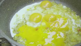 Slow-motion video of breaking chicken eggs into a frying pan with onions,spices and seasonings.Cooking scrambled eggs,Frittata,omelette or fried eggs.Preparation of diet food,proper vegan nutrition