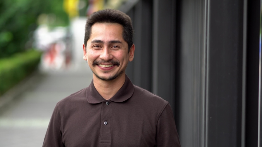 Young man asian smiling and looking at camera. Portrait of a happy handsome young man in a  urban street. Close up face of young cool trendy man looking at camera | Shutterstock HD Video #1060389086