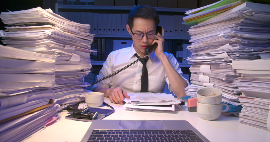 Busy asian business man working multi tasking, talking phone, using laptop, doing paperwork. Tired alone male lay down on desk covered with stack of document at late night.Time lapse, Fast speed shot. Royalty-Free Stock Footage #1060390106