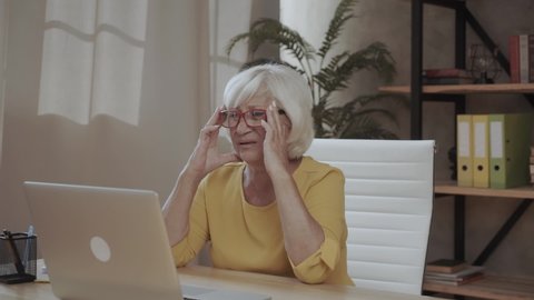 Upset aged woman using laptop at home suffering from headache, tired senior female massaging temples having severe pain or blurry vision, exhausted elderly lady experience dizziness from computer