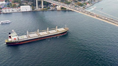 Cargo ship sailing under the Bosporus bridge. A bulk carrier or bulker - a merchant ship specially designed to transport unpackaged bulk cargo, such as grains, ore, coal or timber. Aerial view