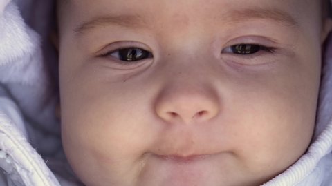 infant, childhood, emotion concept - close-up of cute smiling face of brown-eyed chubby newborn awake toothless baby 6 months old looking at camera lying in white jacket in stroller with drooling lips