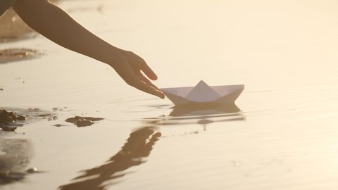 child puts a paper boat into the water. happy family fantasy kid dream concept. child playing with paper boat ship. a child hand launches a boat in a park lifestyle in a pond
