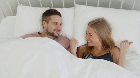 Happy young woman and man falls on the white bed in room. Lovers looking to each other
