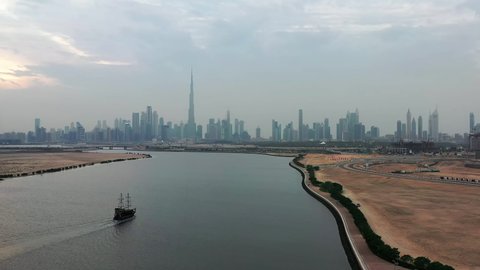 Aerial view of Dubai skyline during cloudy sunset with arab cruise dhow ship flowing in lake towards Burj Khalifa in Downtown Dubai, UAE