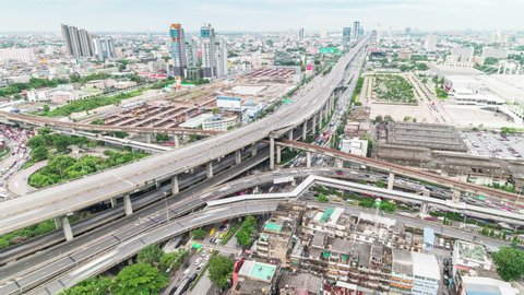 Time-lapse of car traffic transportation on highway, road intersection, sky train railway, under construction site. Urban transport lifestyle, Asian city life. High angle cityscape view zoom out