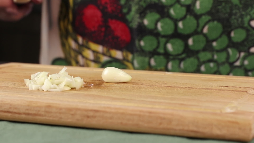 cut garlic with knife above a wooden cutting board, side view