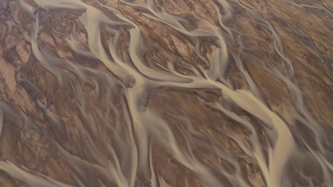 Aerial: Glacial river Meltwater mixed with natural mineral sediment in river deltas creating stunning pattern Iceland Rotating and Tilt up view
