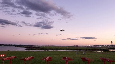 real time fotage of an  Airport at sunset. Video shows a river, the tower, runway, silhouettes of terminal buildings and an airplane taking off and going up.