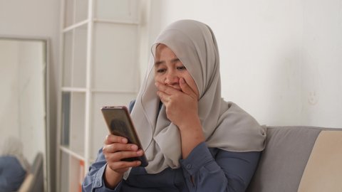 Sad, emotional Asian muslim woman crying and sends a message on mobile phone, bad news on phone concept