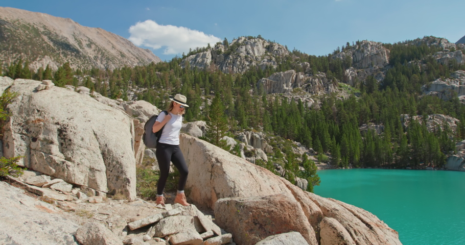 Woman with arms raised on top of mountain looking at scenic blue lake view. Hiker lifting hands up celebrating life with scenic nature landscape view, enjoying wanderlust vacation travel adventure, 4K