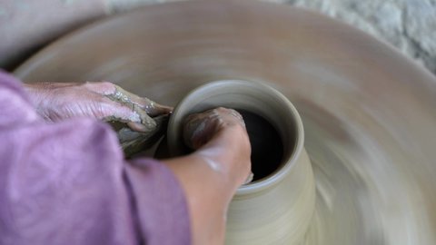 Close-up of a woman potters rotate a wheel with her foot and making a beautiful clay pot with her hands at pottery manufacture in the Old Town Hoi An, Vietnam