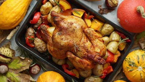 Roasted whole chicken or turkey with pumpkins, pepper and potatoes. With colorful mini pumpkins, autumn leafs and chestnuts served around aged stone dark rustic background, frame. Thanksgiving Day