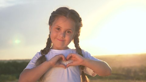 Happy little girl hands holding heart shape. A child at sunset folded his hands in the form of a heart. The girl smiles. Child love symbol of a happy family. Heart sign of family love. Baby smiles