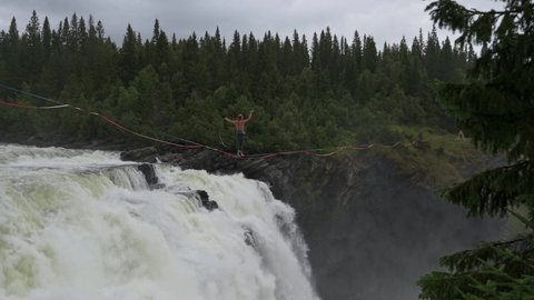 Man walking a tightrope across Tannforsen waterfall in Sweden