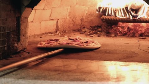 Placing Pizza in Wood fired Pizza with onions and meat. Oven using a pizza peel. Restaurant chef takes pizza in a wood fired oven at traditional restaurant.