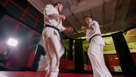 KAZAN, TATARSTAN/RUSSIA - JUNE 30 2020: Sportsmen wearing traditional white kimonos fight kicking by legs in light spacious gym at karate training low angle shot on June 30 in Kazan