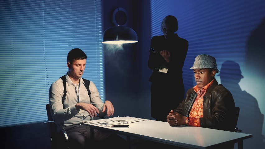 Detectives questioning suspect offender and showing him criminal evidences. Female detective writing notes of the interrogation. | Shutterstock HD Video #1060420567