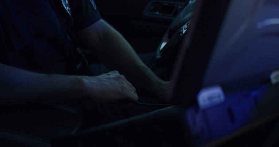 Portrait of police officer talking on CB radio while checking information on a laptop inside a car. Shot on RED Dragon with 2x Anamorphic lens Royalty-Free Stock Footage #1060426225