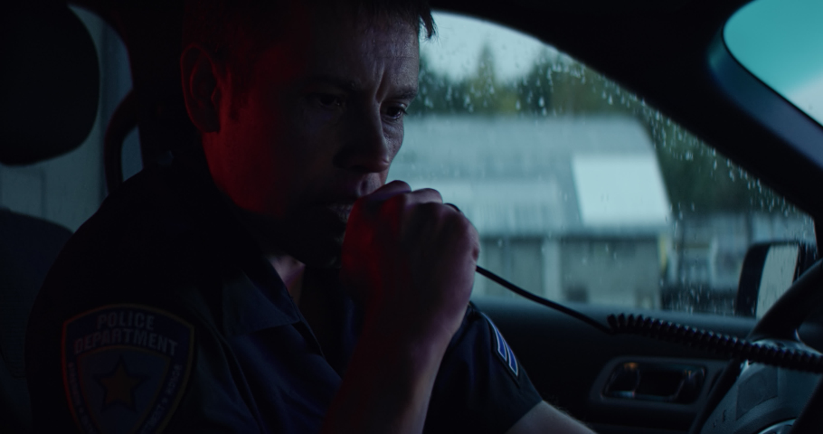 Portrait of police officer talking on CB radio while checking information on a laptop inside a car. Shot on RED Dragon with 2x Anamorphic lens