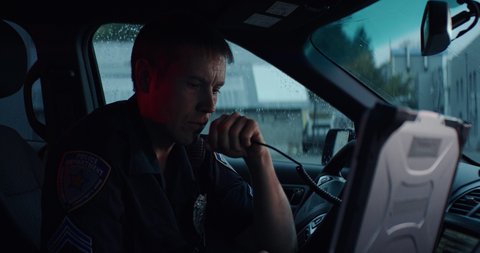 Portrait of police officer talking on CB radio while checking information on a laptop inside a car. Shot on RED Dragon with 2x Anamorphic lens