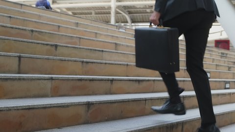 Close up shot of hurry Asian young businessman running up on stair going to work in office. The working man holding business handbag with office formal suit walking outdoor in urban city.