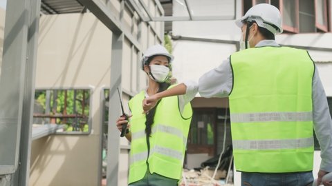 Asian workers people wearing protective face mask onsite of architecture due to covid pandemic crisis. Male and female engineers making elbow touch instead of handshake to avoid coronavirus infection.