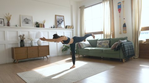 Young Woman doing balance exercise and Stretching sports Yoga, Black Sportswear Leggings and Top, bright room At home in the Morning.