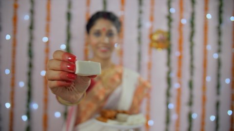 An Indian woman in a traditional Bengali saree eating sweets (Bengali Sandesh). A medium shot a housewife holding a plate of sweets and eating tasty Bengali desserts on the occasion of Durga Puja