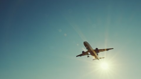 Large airliner with passengers on blue sky is landing on landing strip at airport of bright orange sunset on sunny summer day. Go Everywhere. Airplane flies in sky at sunset day lens flares. Travel
