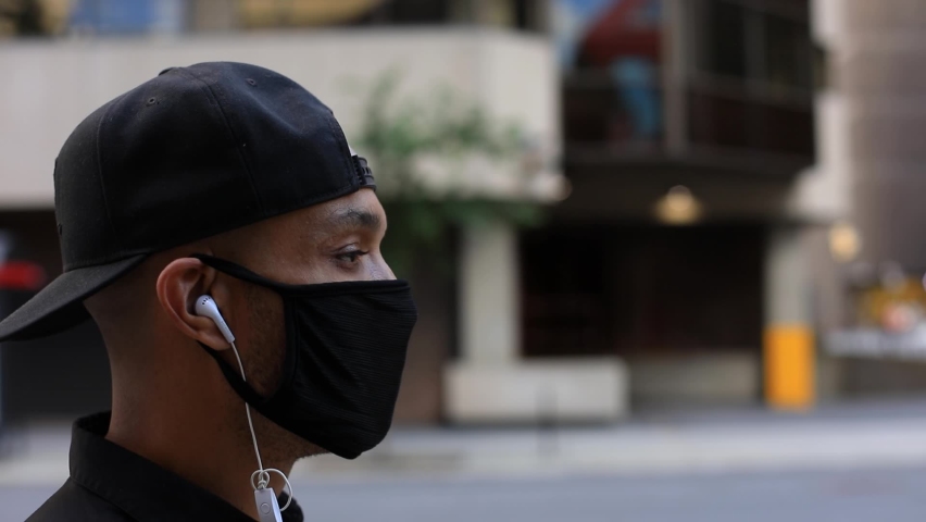 Selective focus of young man with cap listening to music using earphones while walking on pedestrian wearing coronavirus face protection mask Royalty-Free Stock Footage #1060438078