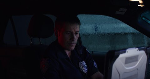 HANDHELD Portrait of police officer talking on CB radio while checking information on a laptop inside a car. Shot on RED Dragon with 2x Anamorphic lens