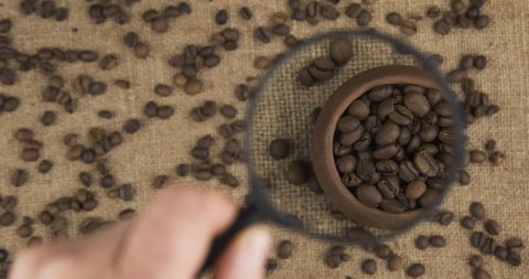 Examining coffee beans with a magnifying glass. Top view. Moving magnifying glass