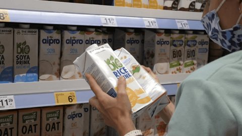 Back view of person reading the labels of bio organic rice milk and soya milk to choose better one. Healthy vegan life style. Warsaw-Poland-2020