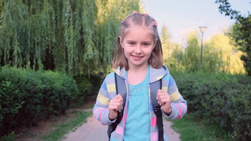 Little girl with backpack going to school through sunny park