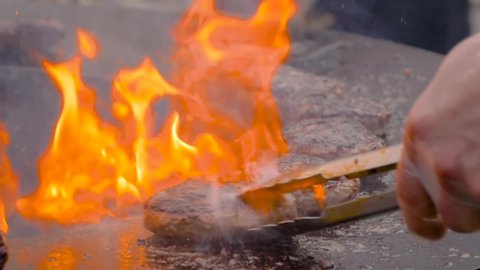 Street food, barbecue, outdoor cooking, gastronomy, cookery concept. Super slow motion: chef grilling fresh meat cutlets for burgers on brazier with hot flame at summer local food market - close up