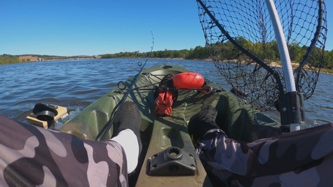 View from inside of motorized kayak while cruising upstream. Fisherman camo pants and legs visible with landing net and fishing rod and anchor in front.