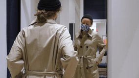 Inside the changing room. Caucasian woman with protective mask on a face checking in the mirror if classic trench coat fits her - Powered by Shutterstock - Get 15% off with code: PIKWIZARD15