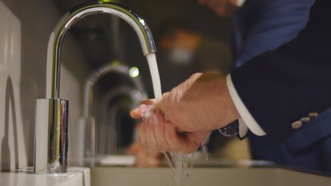 Close up of businessman washing hands in sink in public restroom. Entrepreneur disinfecting hands with soap and water after visiting office toilet