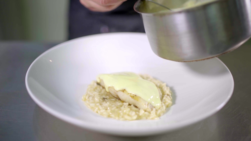chef placing hollandaise sauce on risotto in stainless steel kitchen