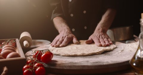 Senior professional italian restaurant chef working, shaping floured dough for pizza. Experienced cooker making pizza using traditional recipe, isolated on black background close up 4k footage