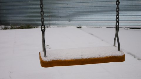 An empty swing covered with snow sways in the wind