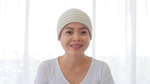 Asian female cancer patient wearing headscarf smiling and look at camera on white background. Breast cancer concept.
