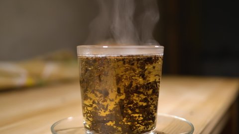 Cup of Freshly Brewed Black Tea on Wooden Table, Escaping Steam, Warm Soft Light, Darker Background. Freshly Brewed Black Tea in Transparent Glass Cup, Escaping Steam. Teatime Ceremony Zen Relaxation.