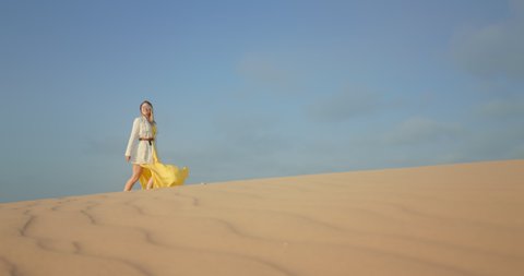 4K slow motion footage with blue space for copy or text on background for commercial usage. Cinematic shot of woman in stylish outfit walking by wavy sand surface. Scenic wild nature landscape view