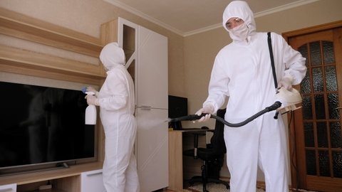 Team of doctors in protective face masks and protective suits conduct disinfection in an apartment with a patient with a coronavirus.