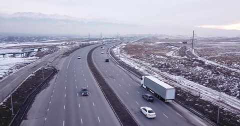 A large truck is traveling on a multi-lane highway. Around the steppe, snow and emptiness. Cloudy weather, winter. The trucker continues on his way. Cars overtake. Transport company. Kazakhstan.