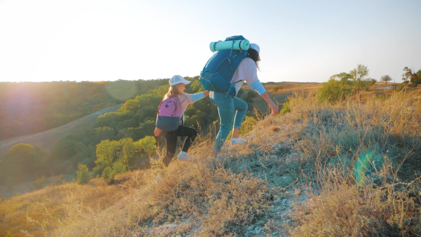 Mother and daughter with backpacks running through the meadow at sunset. Family tourism concept.